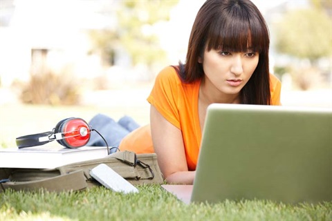 woman lying on grass looking at a laptop